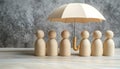 Human figures under umbrella on light wooden table. Insurance concept Royalty Free Stock Photo