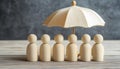 Human figures under umbrella on light wooden table. Insurance concept Royalty Free Stock Photo