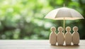 Human figures under umbrella on light wooden table. Insurance concept Royalty Free Stock Photo