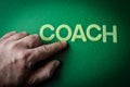 Human finger pointing the word Coach written with plastic letters on green paper background