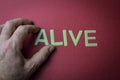 Human fingers holding the word Alive written with plastic letters on dark red paper background Royalty Free Stock Photo