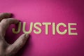 Human fingers holding the word Justice written with plastic letters on bright pink paper background