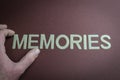 Human fingers holding the word Memories written with plastic letters on brown paper background