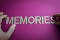 Human fingers holding the word Memories written with plastic letters on pink paper background