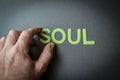 Human fingers holding the word Soul written with plastic letters on dark gray paper background Royalty Free Stock Photo