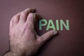 Human fingers removing the word Pain written with plastic letters on brown paper background