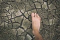 Human foot on dried cracked lifeless earth. Man`s barefoot on dry soil with dead plants. Barren land because of ecological