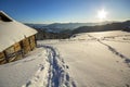 Human footprint path in white deep snow leading to small old wooden forsaken shepherd hut in mountain valley, spruce forest, woody