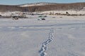 Human footprints lead to the rural shore along the frozen snow-covered surface of a large lake Royalty Free Stock Photo