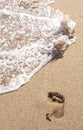 Human footprints on the sand with sea water. Foam from a wave on the sand. Royalty Free Stock Photo
