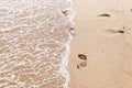 Human footprints on the sand with sea water. Foam from a wave on the sand with traces.