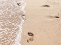 Human footprints on the sand with sea water. Foam from a wave on the sand with traces. Royalty Free Stock Photo