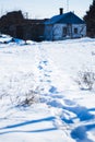 Human footprints in the snow, winter path in the field leading to the small rural house