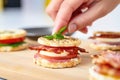 human hand adding bacon slice to an english muffin sandwich