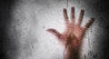 Human hand behind a wet frosted glass, dark grungy horror concept