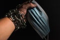 Human hand chained in chains holds a medical protective mask, isolated on black background