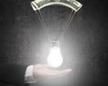 Human hand holding bright light bulb with money parachute. Royalty Free Stock Photo