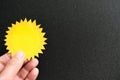 Human hand holding bright yellow sun cutout in black background. Light amidst darkness concept