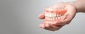 Human Hand Holding Complete Upper and Lower Denture Set on Neutral Background - Dental Prosthesis