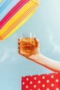 Human hand holding glass of whiskey over summer blue sky background. Vacation, happiness, summer vibes and ad concept