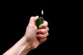 Human hand holding green lighter with burning flame on black backdrop.  on black background Royalty Free Stock Photo