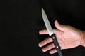 Human hand holding a knife in dark black background. Murder, killer and suicide concept.