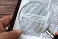 Human hand holding magnifying glass over open holy bible book of Exodus verses for Ten Commandments, top view