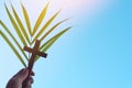 Human hand holding palm leaves with wooden crucifix cross in clear blue sky. Palm sunday background. Royalty Free Stock Photo