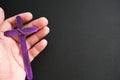 Human hand holding a purple wooden cross in black background. Nurture, care and love christian faith concept. Royalty Free Stock Photo