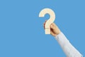 Human hand holding question mark against blank blue background for FAQ and answers