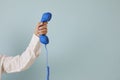 Human hand holding blue landline phone receiver on light blue copy space background Royalty Free Stock Photo