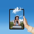 A human hand holding tablet with a screen view of an Asian girl in a hat and a suitcase with a mountain view and blue sky Royalty Free Stock Photo