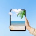 Human hand holding tablet with a screen view of the beach with an ocean view and blue sky Royalty Free Stock Photo