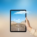 Human hand holding tablet with a screen view of a street with hills and rock cliff view with blue sky Royalty Free Stock Photo