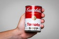 Human hand holding a tin can of Capbell`s Soup tomato soup