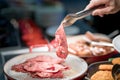 Human hand holding tongs over plate of sliced smoked meat in bar