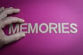 Human hand holding the word Memories written with plastic letters on pink paper background