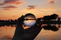 The human hand that holds a glass ball in which the sunset is reflected against the sunset over the lake Royalty Free Stock Photo