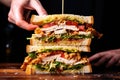 human hand layering sliced chicken on a club sandwich