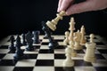 Human hand is playing chess and defeats the king, checkmate on the chessboard against a black background Royalty Free Stock Photo