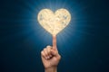 Human hand pointing towards a glowing heart shaped object with intricate patterns against a deep blue background Royalty Free Stock Photo