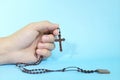 Human hand praying and holding a scapular rosary in blue background. Christianity and Catholicism concept. Royalty Free Stock Photo