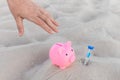 A human hand takes a piggy bank next to an hourglass against the background of white beach sand. Money, investments and fanance Royalty Free Stock Photo