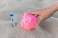 A human hand takes a piggy bank next to an hourglass against the background of white beach sand. Money, investments and fanance Royalty Free Stock Photo