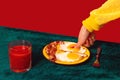Human hand tasting bacon and eggs isolated on green and red background. Vintage, retro style interior. Food pop art