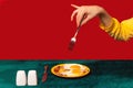 Human hand tasting bacon and eggs isolated on green and red background. Vintage, retro style interior. Food pop art
