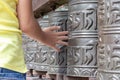 Human hand touching, rotating nepalese traditional metal prayer wheels hanging in a row