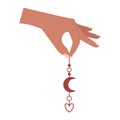 A human hand with two fingers holds an earring with a crescent moon and a heart, a boho element. A symbol of love, romance,