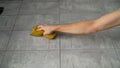 A human hand uses a yellow sponge on a ceramic tile floor. Cleaning tiles after renovation, hand with sponge close-up. A Royalty Free Stock Photo