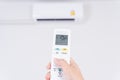 Human hand is using white remote of air conditioner for turn on or adjust temperature of air conditioner inside the room